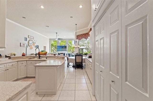 kitchen featuring white cabinets, a sink, open floor plan, light tile patterned floors, and ornamental molding