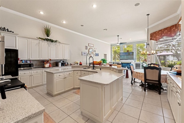 kitchen with a kitchen island with sink, a sink, stainless steel microwave, ornamental molding, and light tile patterned flooring