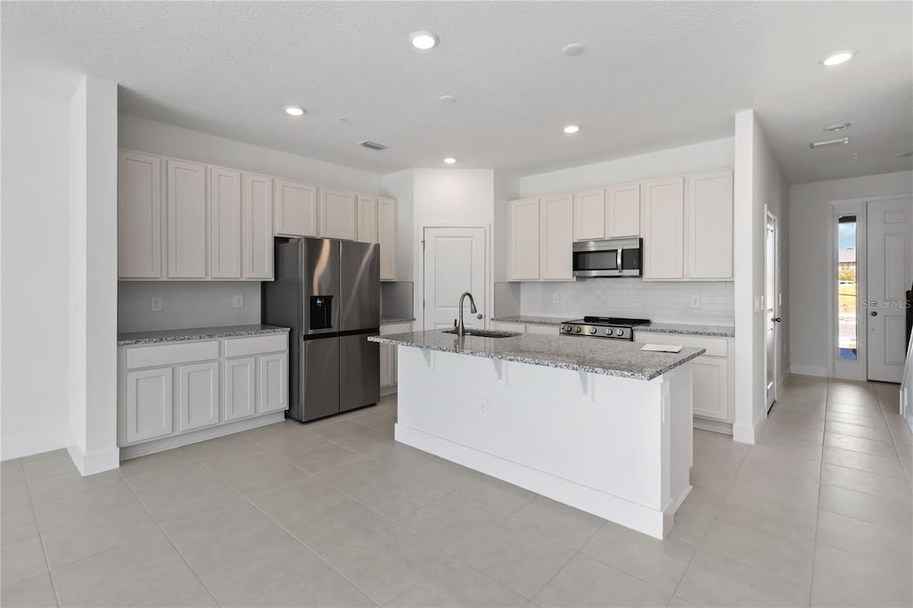 kitchen with a kitchen bar, appliances with stainless steel finishes, a sink, light stone counters, and an island with sink