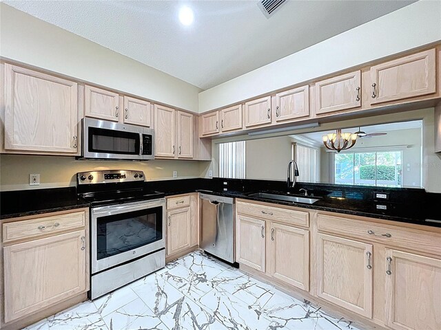 kitchen featuring stainless steel appliances, a sink, light brown cabinetry, dark countertops, and light marble finish flooring