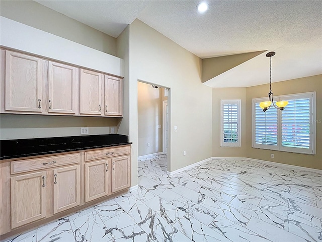 kitchen with a chandelier, light marble finish flooring, dark countertops, a textured ceiling, and hanging light fixtures
