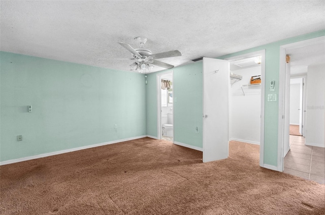unfurnished bedroom featuring a walk in closet, a textured ceiling, a closet, carpet flooring, and ensuite bath