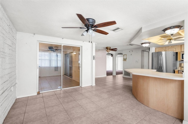 kitchen featuring visible vents, freestanding refrigerator, ceiling fan, arched walkways, and light tile patterned floors
