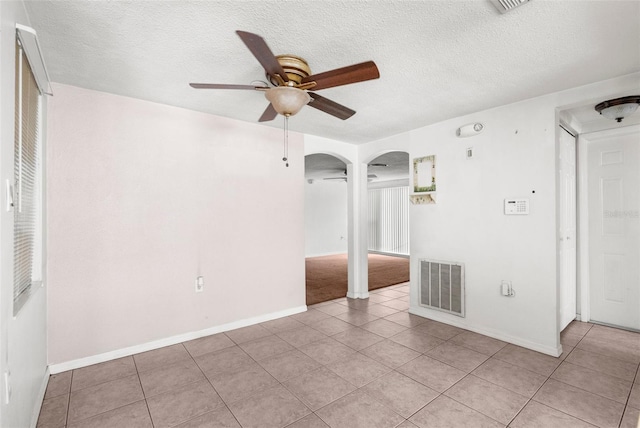 empty room featuring a ceiling fan, arched walkways, visible vents, and light tile patterned floors