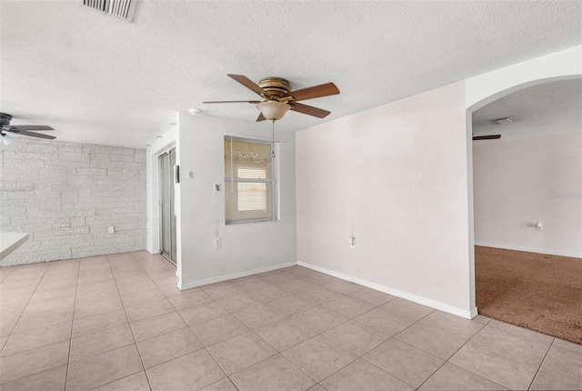 spare room with visible vents, light tile patterned flooring, a textured ceiling, arched walkways, and a ceiling fan
