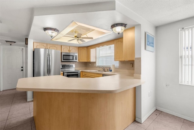 kitchen with light brown cabinetry, appliances with stainless steel finishes, a sink, light countertops, and light tile patterned floors