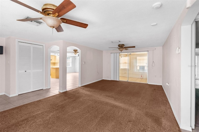 unfurnished living room featuring ceiling fan, tile patterned flooring, carpet floors, arched walkways, and baseboards