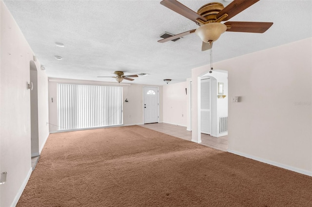 unfurnished living room with baseboards, arched walkways, ceiling fan, and light carpet