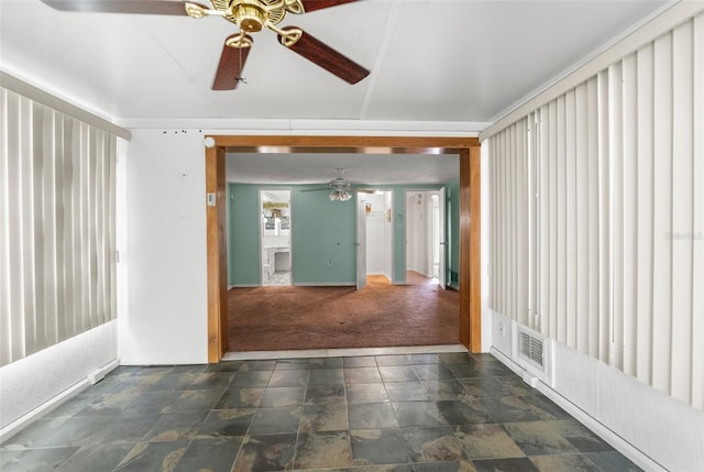 spare room featuring baseboards, stone finish floor, a ceiling fan, and dark carpet