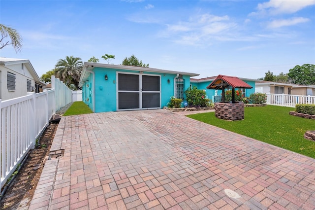 view of front of house with fence private yard, decorative driveway, a gazebo, a front lawn, and stucco siding