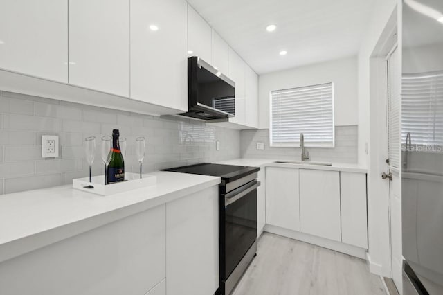 kitchen with a sink, light countertops, white cabinetry, decorative backsplash, and range with electric stovetop