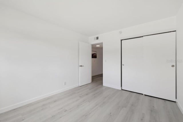 unfurnished bedroom with baseboards, a closet, light wood-type flooring, and visible vents