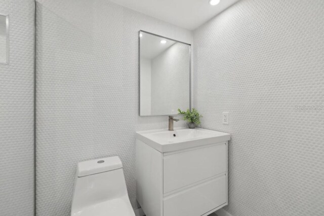 half bath featuring toilet, tile walls, recessed lighting, and vanity