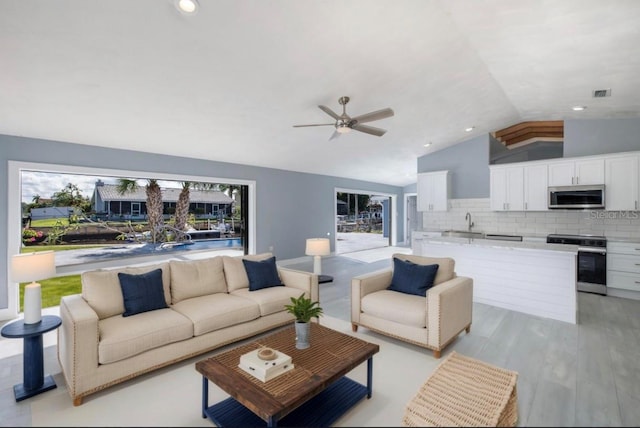 living area with a ceiling fan, vaulted ceiling, light wood finished floors, and visible vents