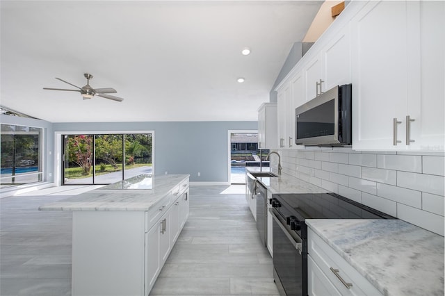 kitchen with decorative backsplash, a kitchen island, ceiling fan, a sink, and stainless steel appliances