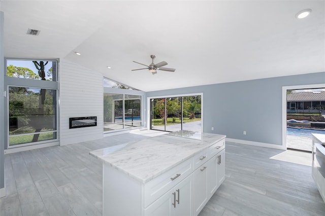 kitchen with ceiling fan, a center island, a large fireplace, light stone counters, and a wealth of natural light