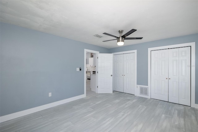 unfurnished bedroom with multiple closets, baseboards, light wood-type flooring, and visible vents