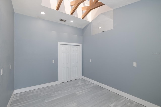 spare room featuring visible vents, a towering ceiling, baseboards, light wood-style floors, and recessed lighting