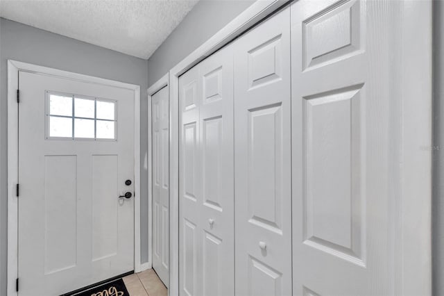 doorway to outside with baseboards, a textured ceiling, and light tile patterned floors