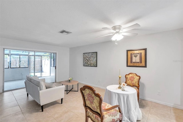 living area with a ceiling fan, a textured ceiling, visible vents, light tile patterned floors, and baseboards