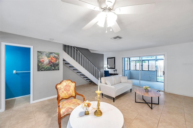 living area featuring ceiling fan, visible vents, stairway, light tile patterned floors, and baseboards
