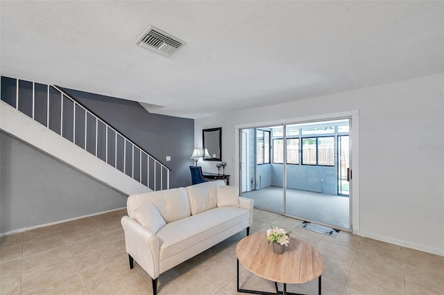 living area featuring tile patterned flooring, a textured ceiling, stairs, baseboards, and visible vents