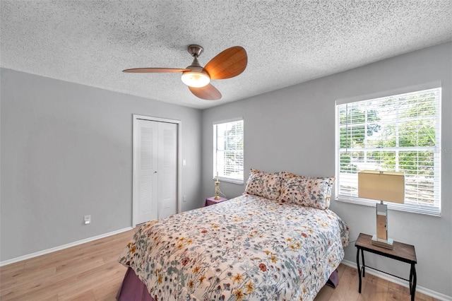 bedroom featuring light wood-style floors, a textured ceiling, ceiling fan, and a closet