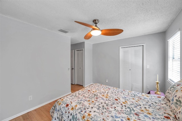 bedroom with a textured ceiling, visible vents, baseboards, light wood finished floors, and multiple closets