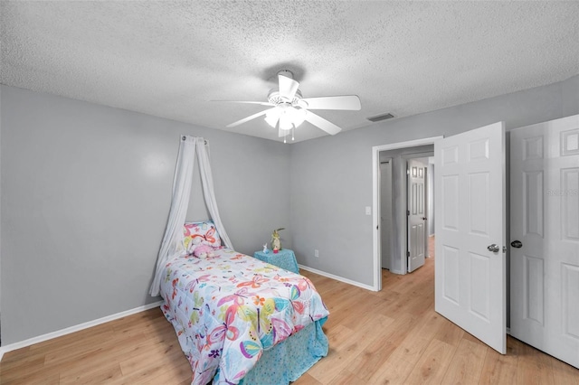 bedroom with a textured ceiling, baseboards, visible vents, and light wood finished floors