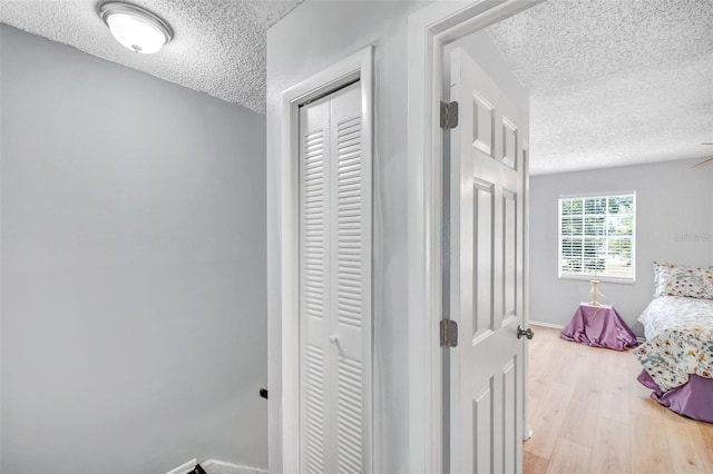 bedroom featuring a textured ceiling, baseboards, light wood finished floors, and a closet