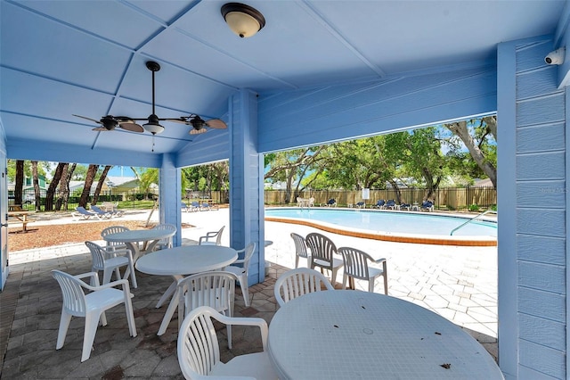 view of patio with a fenced backyard, a community pool, ceiling fan, and outdoor dining space
