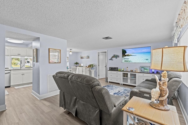 living room with light wood-style flooring, a textured ceiling, and visible vents