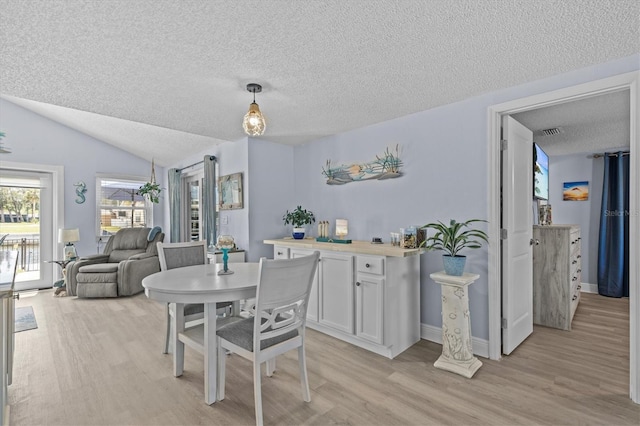 dining space with a textured ceiling, visible vents, lofted ceiling, and light wood-style floors