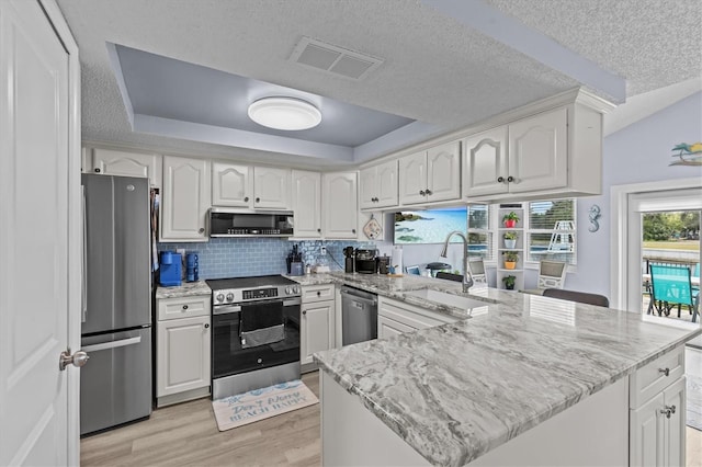 kitchen featuring visible vents, appliances with stainless steel finishes, light wood finished floors, a peninsula, and a tray ceiling