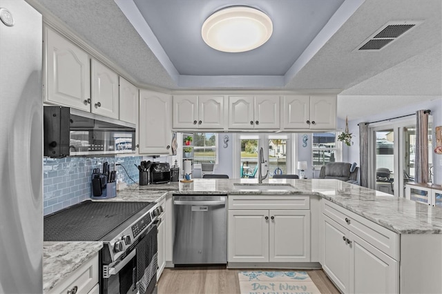 kitchen featuring white cabinets, a sink, stainless steel appliances, a tray ceiling, and visible vents