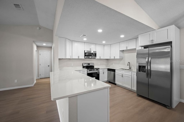 kitchen featuring appliances with stainless steel finishes, a sink, a textured ceiling, a peninsula, and baseboards
