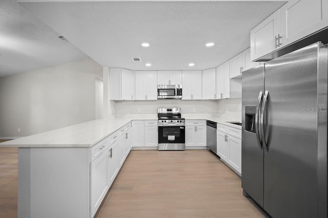 kitchen with appliances with stainless steel finishes, light wood-style flooring, a peninsula, white cabinetry, and recessed lighting