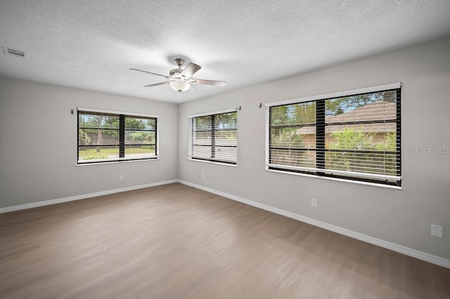 empty room featuring a ceiling fan, a textured ceiling, visible vents, and wood finished floors