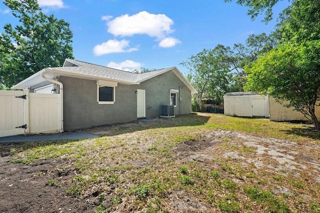 rear view of house featuring fence, a storage shed, stucco siding, cooling unit, and an outdoor structure