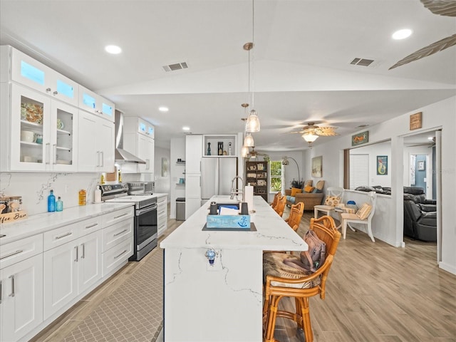kitchen with stainless steel appliances, wall chimney range hood, visible vents, light wood finished floors, and open floor plan