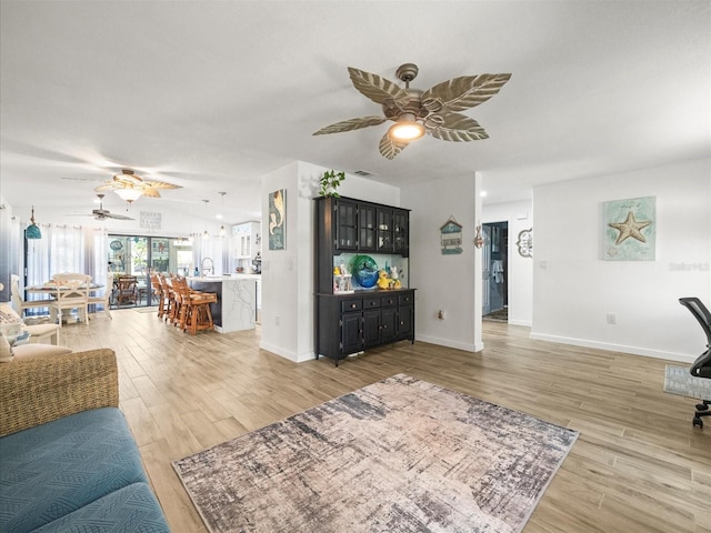 living area with a ceiling fan, baseboards, light wood finished floors, and visible vents