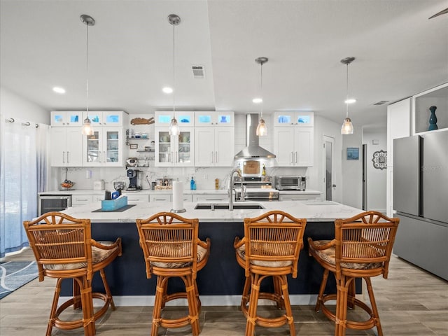 kitchen with a sink, wall chimney exhaust hood, stainless steel appliances, a toaster, and a kitchen island with sink