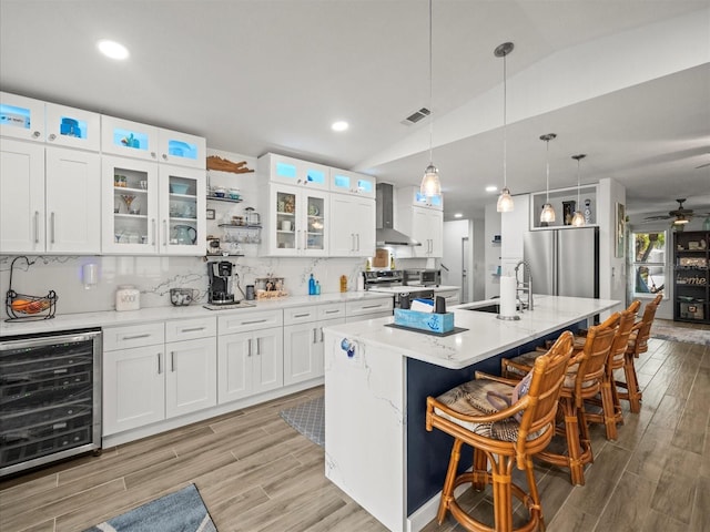 kitchen with a sink, stainless steel appliances, visible vents, wall chimney range hood, and wine cooler