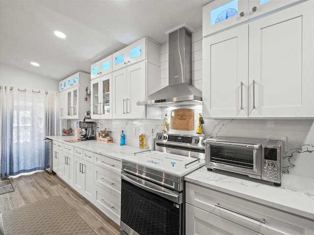 kitchen with a toaster, stainless steel electric stove, white cabinetry, wall chimney exhaust hood, and backsplash
