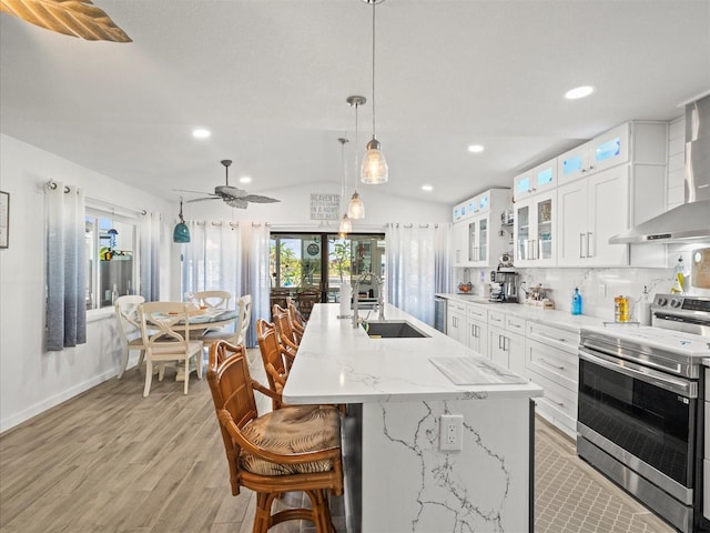 kitchen with stainless steel range with electric stovetop, a sink, a center island with sink, wall chimney range hood, and light wood-style floors