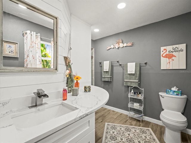 bathroom featuring toilet, wood finished floors, vanity, recessed lighting, and baseboards