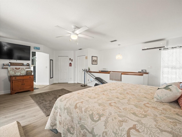 bedroom featuring a ceiling fan, a wall mounted air conditioner, baseboards, light wood finished floors, and visible vents