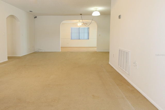 unfurnished room with light carpet, arched walkways, baseboards, and visible vents