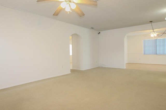 spare room with arched walkways, light colored carpet, and a ceiling fan