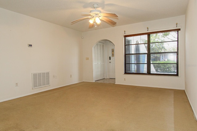 unfurnished room with light colored carpet, visible vents, ceiling fan, arched walkways, and baseboards